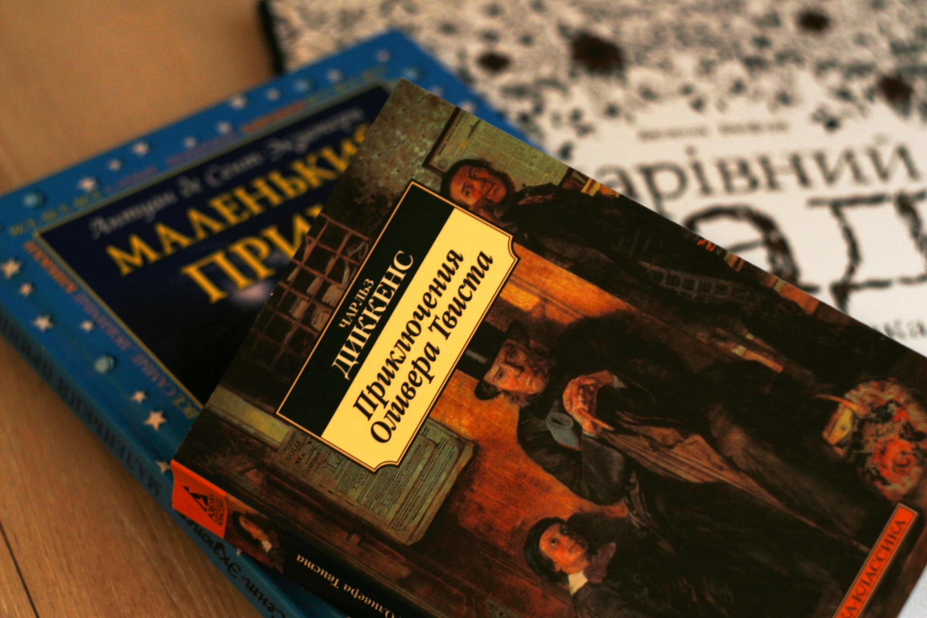 A close-up of three books with titles in Ukrainian, including 'Приключения Оливера Твиста' by Charles Dickens, arranged on a wooden surface.